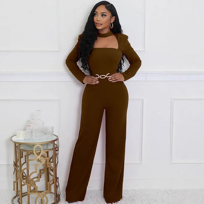 Woman wearing a brown jumpsuit standing in a room with a decorative table.