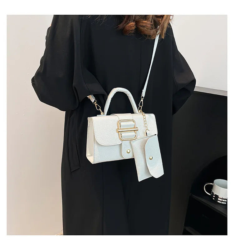 White handbag with gold accents worn by a person in a black coat.