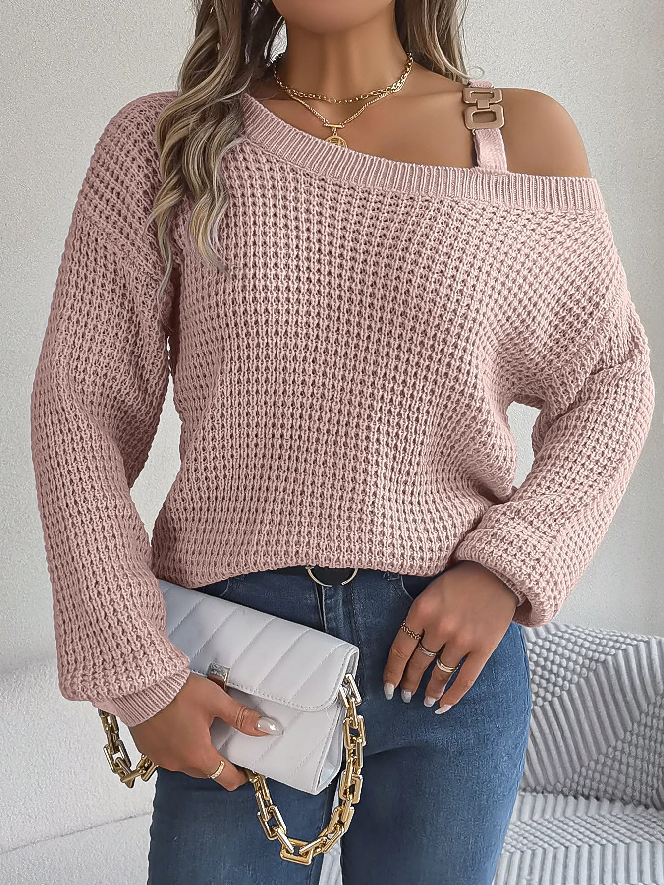Person wearing a pink off-shoulder sweater holding a white clutch with gold chain.