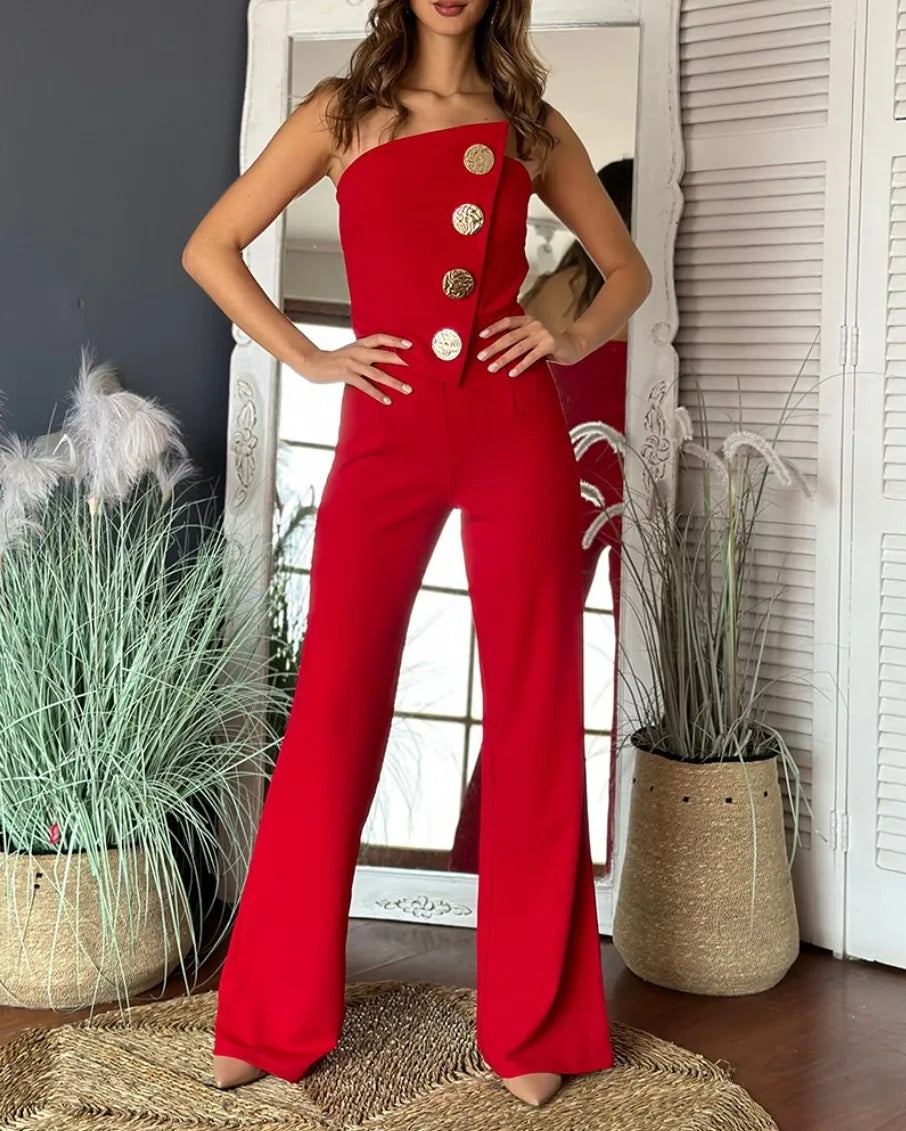 Woman wearing a red jumpsuit with gold buttons in a room with plants and a mirror.