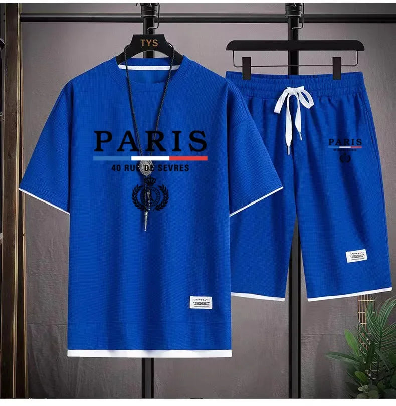 Blue 'PARIS' t-shirt and shorts set on hangers against a gray background