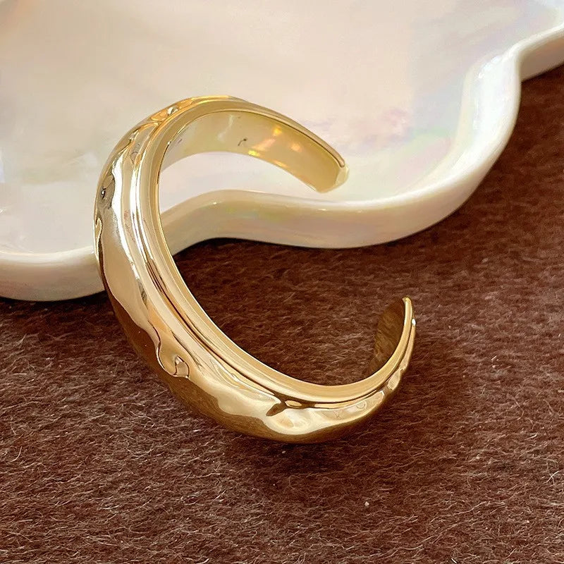 Gold crescent moon-shaped earring on a brown surface with a white dish in the background