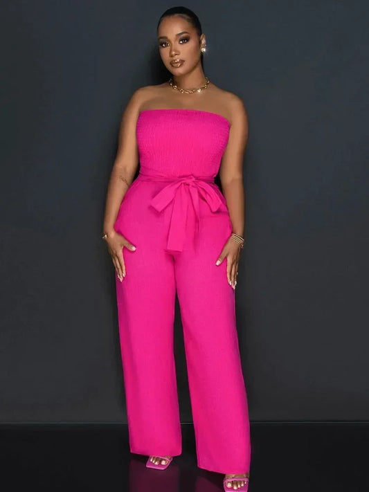Woman wearing a bright pink strapless jumpsuit against a dark background