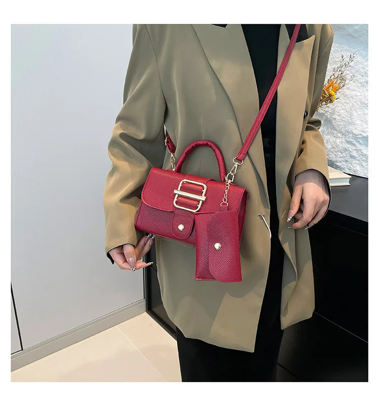 Red handbag with gold accents held by a person wearing a beige coat.