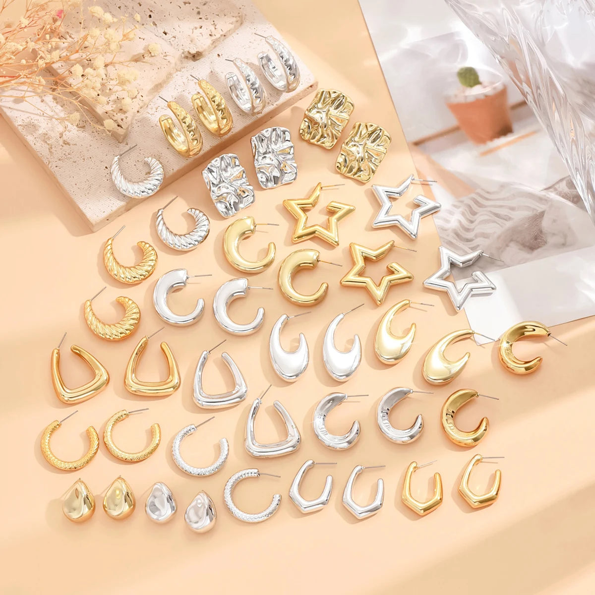 Collection of gold, silver, and rose gold earrings on a beige surface.