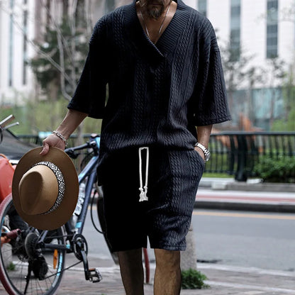 Person wearing a dark knit outfit holding a brown hat on a city street.