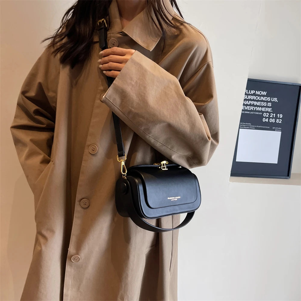 Person wearing a beige coat holding a black handbag against a plain background