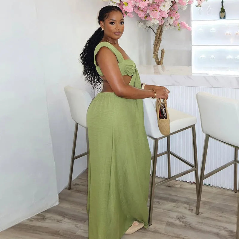 Woman in a green dress standing in a modern kitchen with white chairs and a vase of flowers.
