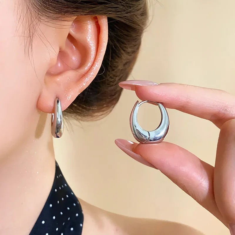 Silver hoop earring being held near an ear with a plain background