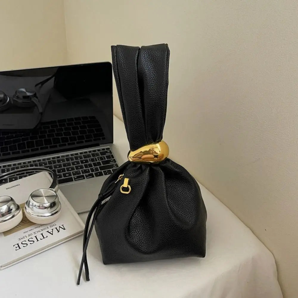 Black drawstring bag with a gold accent on a surface next to a laptop and books.