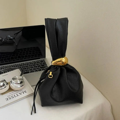 Black drawstring bag with a gold accent on a surface next to a laptop and books.