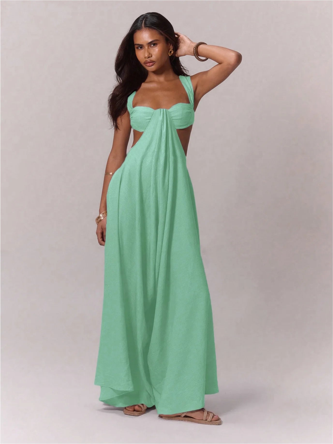 Woman wearing a mint green dress with cut-out sides on a plain background