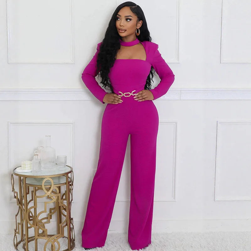 Woman wearing a bright pink jumpsuit standing in a room with a white wall and decorative table.