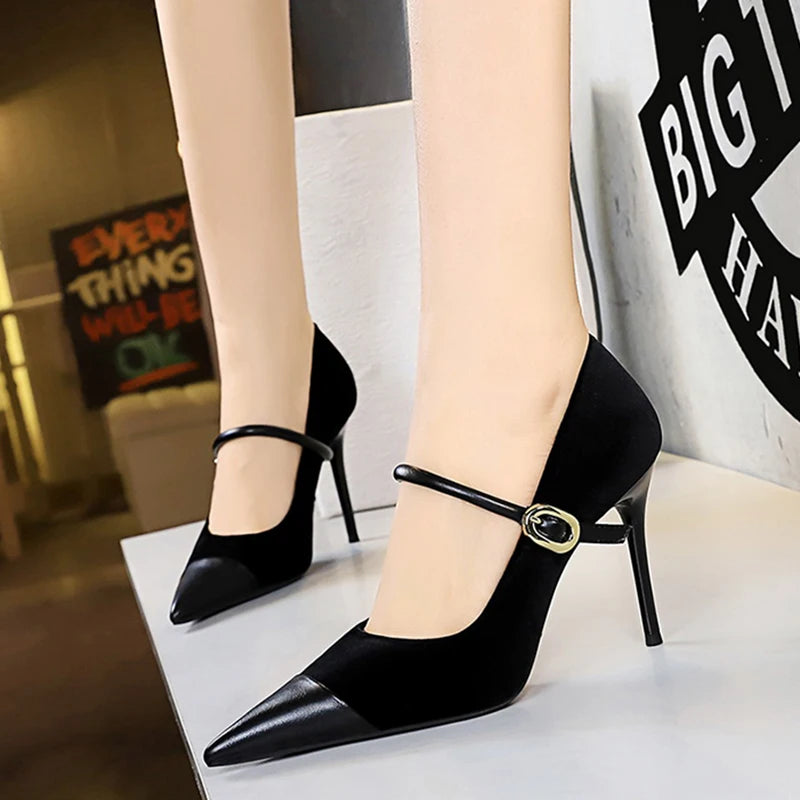 Black high-heeled shoes with a gold buckle worn by a person indoors.