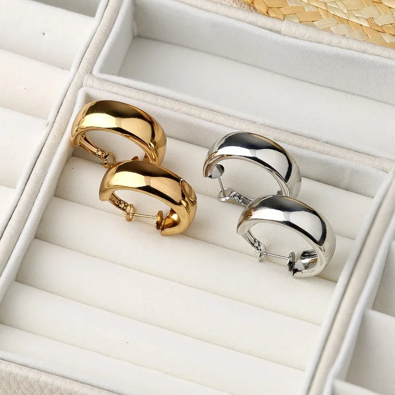 Four huggie hoop earrings in polished gold and silver finishes, displayed on a white jewelry organizer tray.