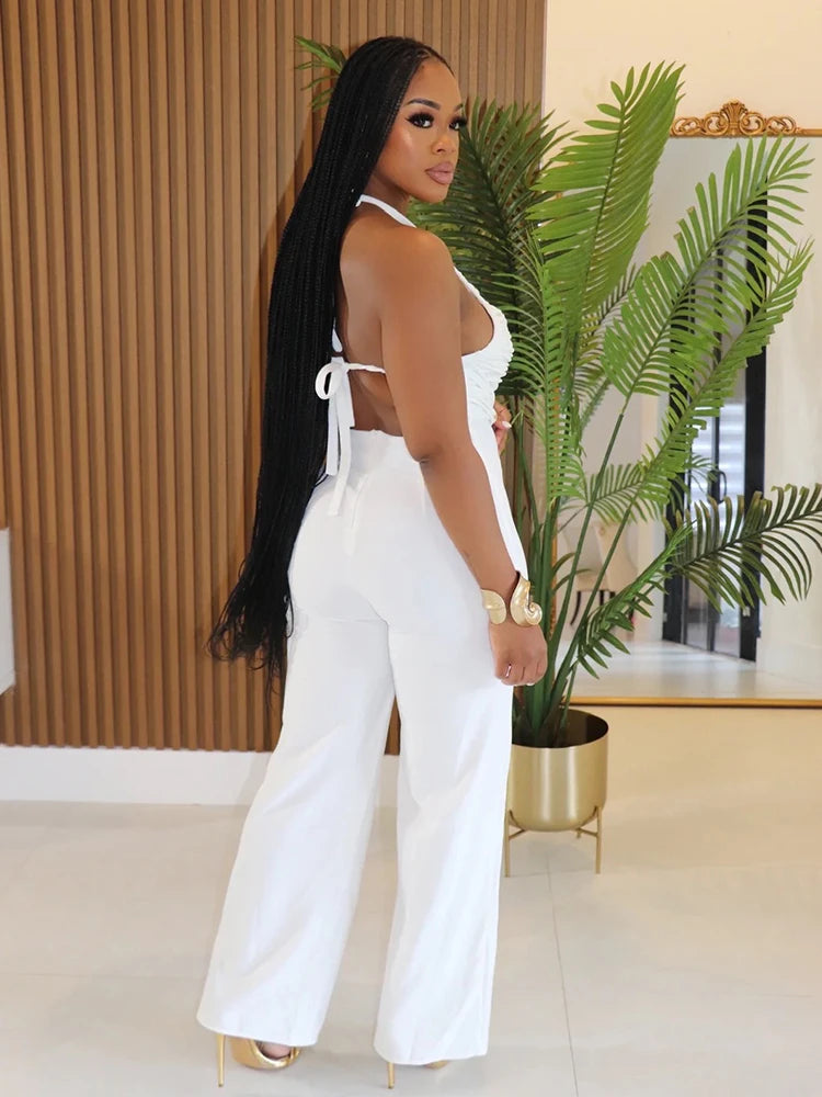 Woman in a white outfit standing in a room with plants and a mirror.