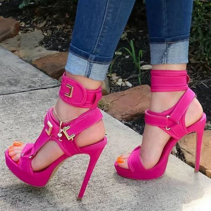 Hot pink high-heeled sandals worn with blue jeans on a stone surface.