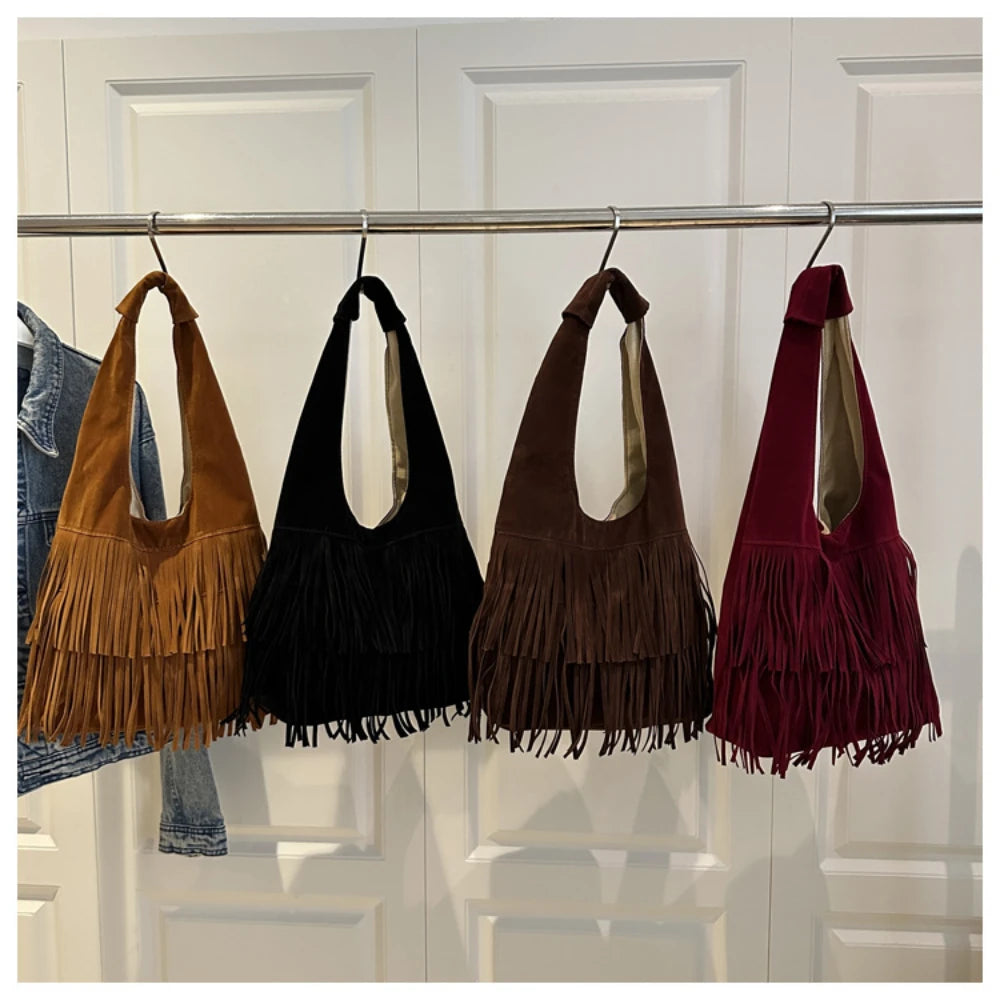 Four handbags with fringe details hanging on a rack against a white wall.