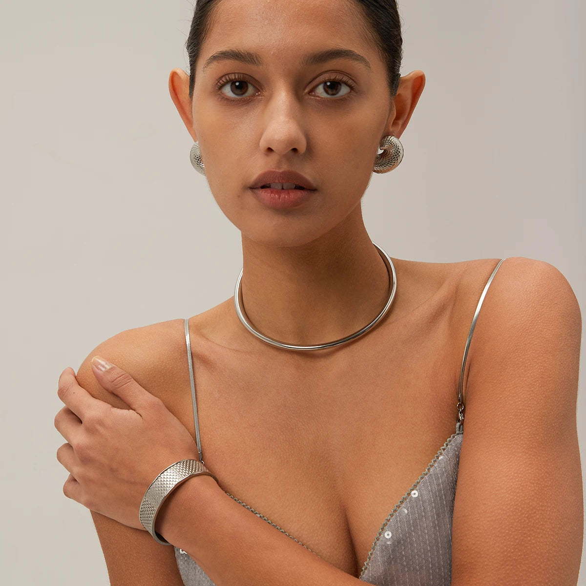 Woman wearing silver jewelry including earrings, necklace, and bracelet against a neutral background