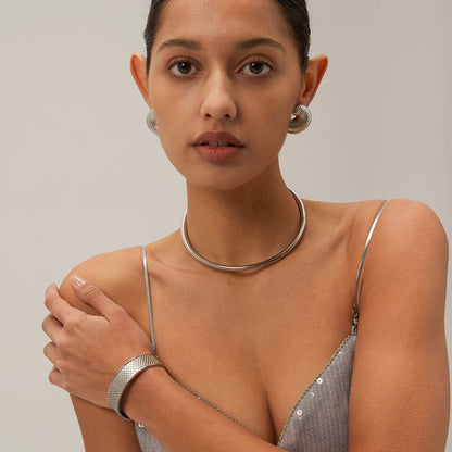 Woman wearing silver jewelry including earrings, necklace, and bracelet against a neutral background