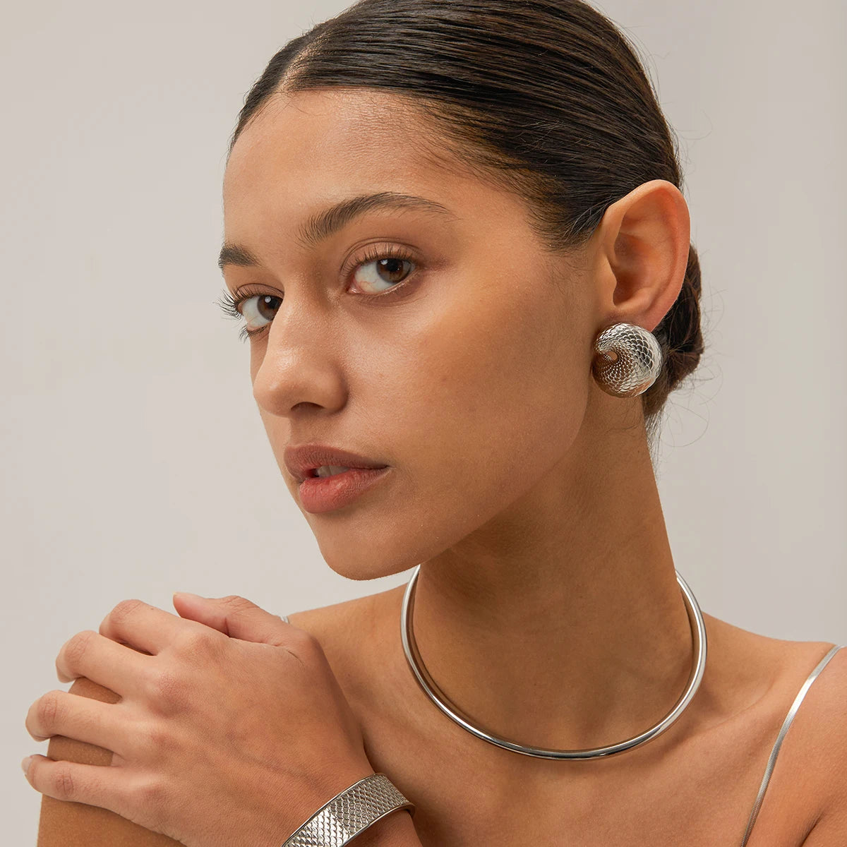 Woman wearing silver jewelry including earrings, necklace, and bracelet against a neutral background