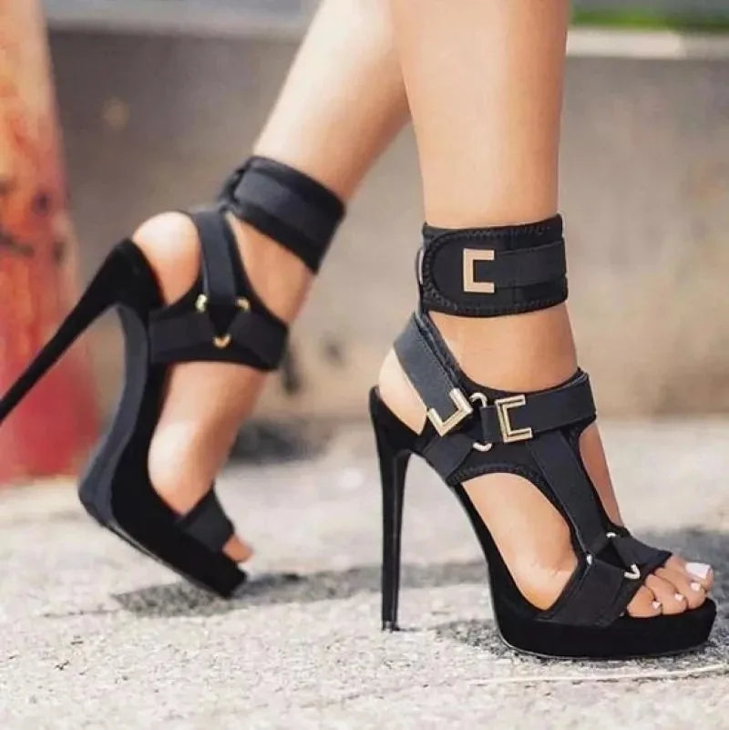 Black high-heeled sandals with gold buckles worn by a person on a blurred background