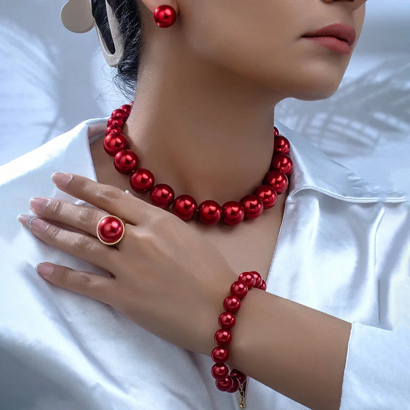 Red pearl necklace, earrings, and bracelet worn by a person on a white background