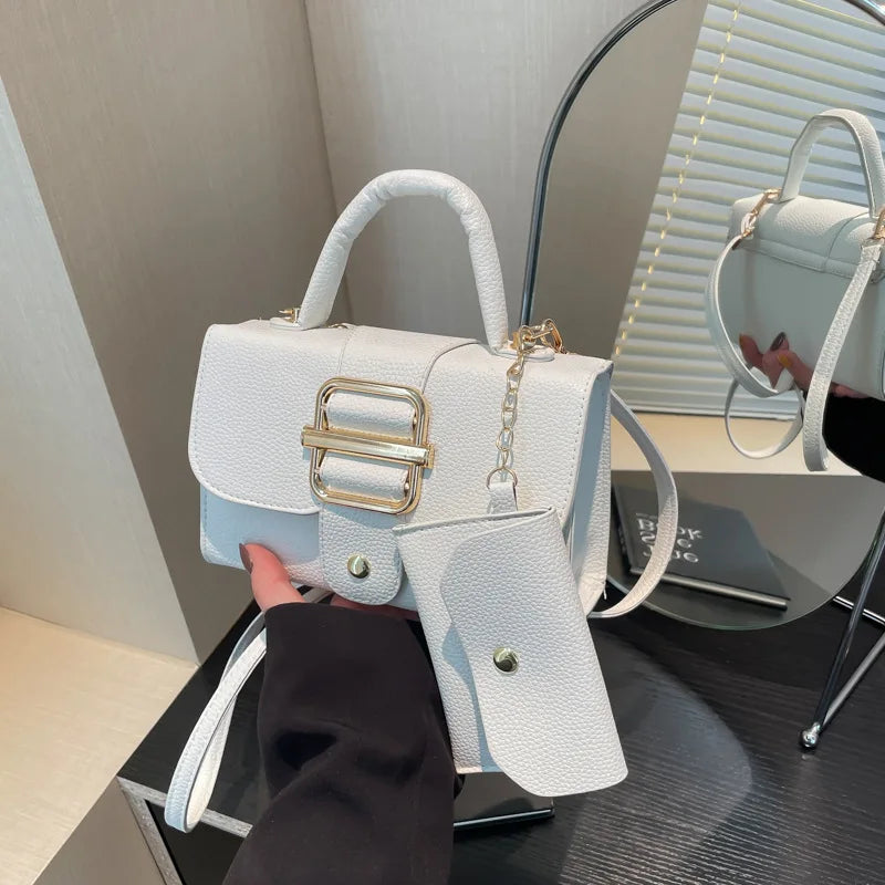 White handbag with gold accents held by a person, with a mirror reflection in the background.