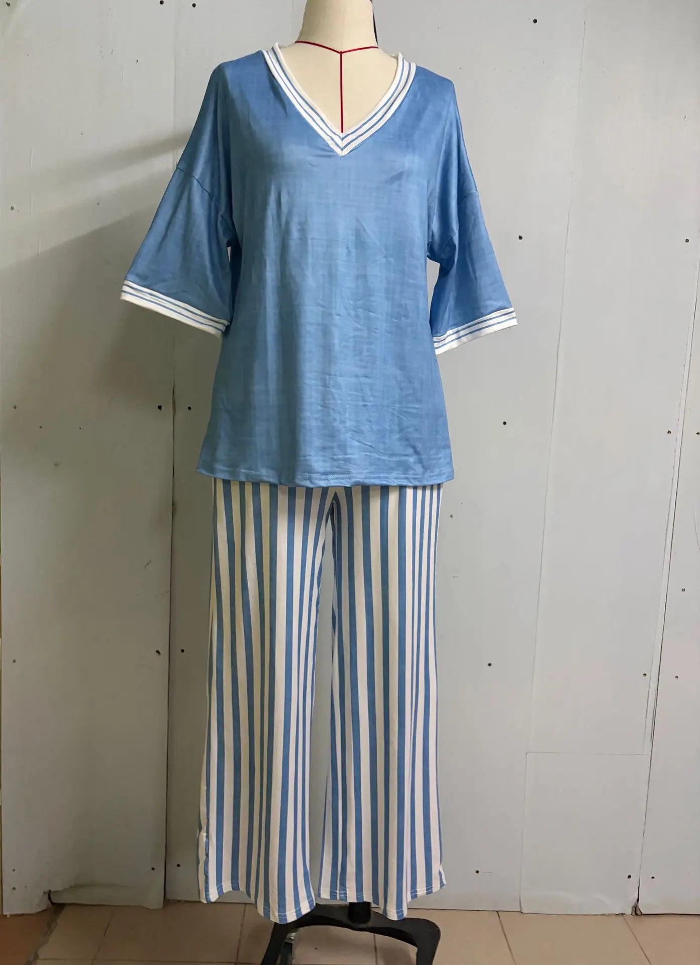 A two-piece pajama set displayed on a mannequin, featuring a light blue short-sleeve V-neck top with white trim and matching blue-and-white vertically striped pants.