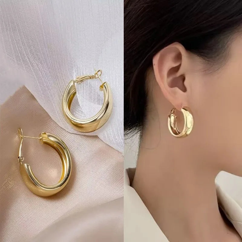 Two polished gold hoop earrings shown on a soft beige fabric background, alongside a close-up of a model wearing one earring.