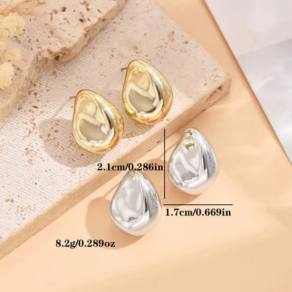 Gold and silver teardrop-shaped earrings on a textured beige surface with measurements.
