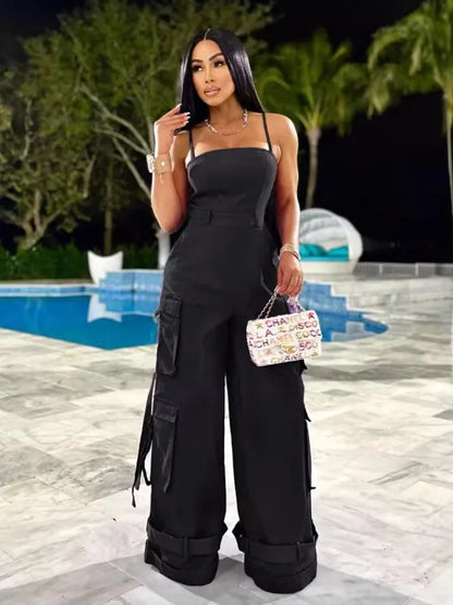 Woman in a black jumpsuit holding a colorful handbag by a pool at night.