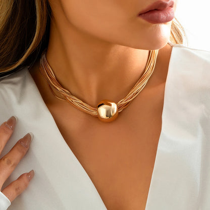 Gold-tone multi-strand statement chain necklace with a polished rounded centerpiece, styled with a white V-neck blouse.