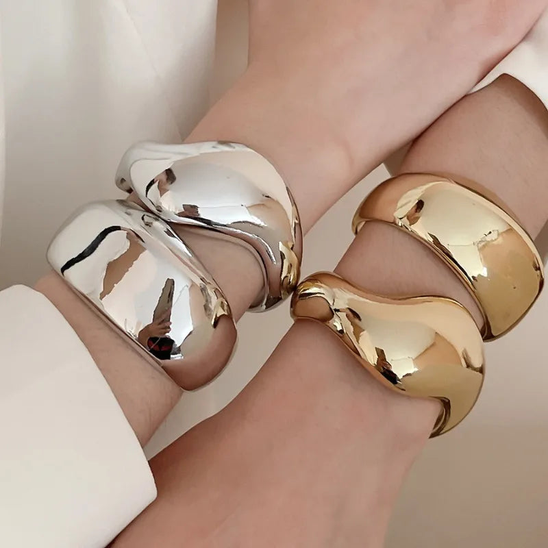 Gold and silver cuff bracelets on a person's wrist against a neutral background