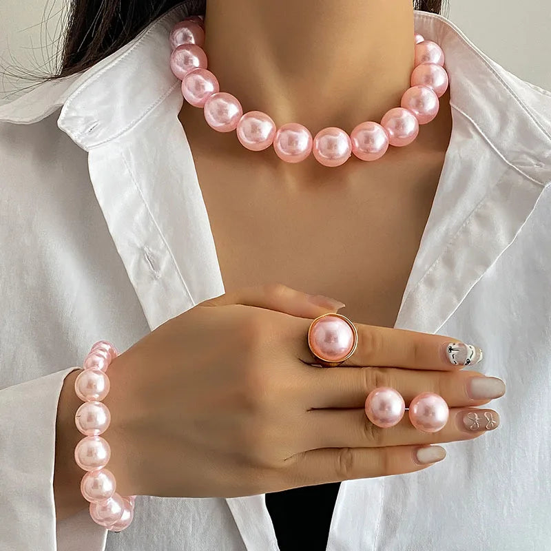 Person wearing a pink pearl necklace, bracelet, and ring with a white shirt.