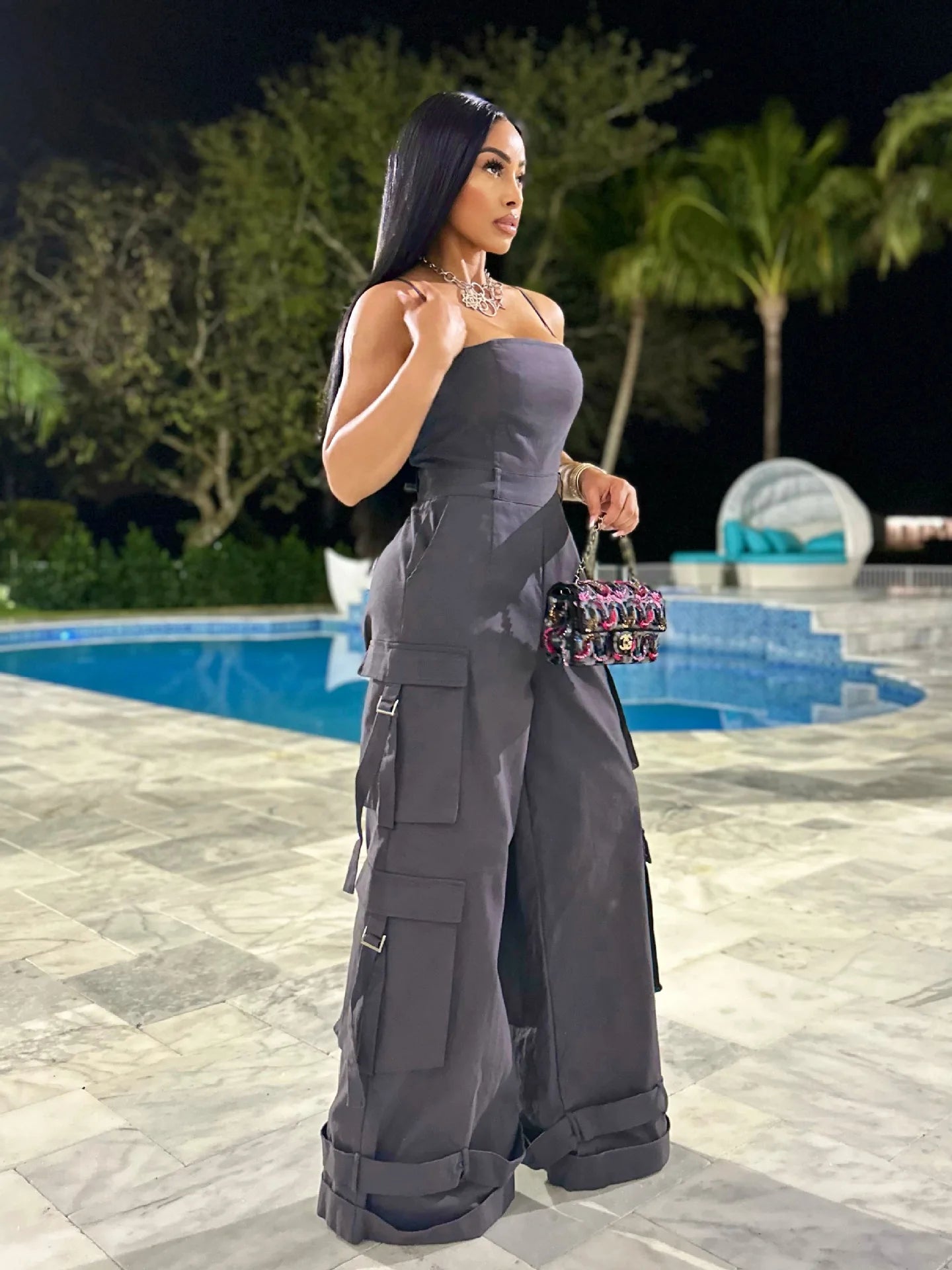 Woman in a gray outfit standing by a pool at night