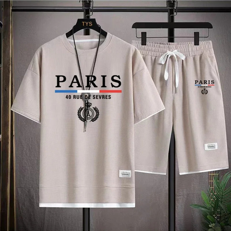 Beige t-shirt and shorts set with 'PARIS' branding on hangers against a gray background.