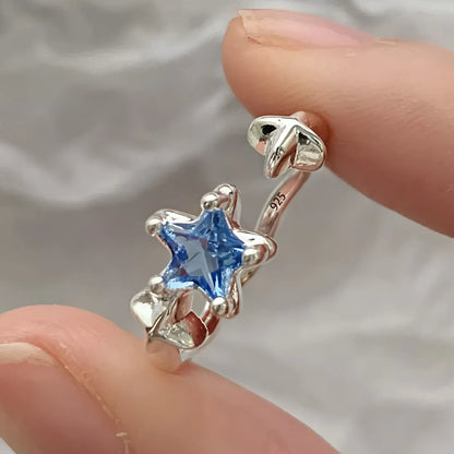 Silver earring with a blue gemstone held between fingers against a neutral background
