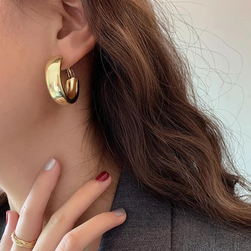 Close-up of a person wearing gold hoop earrings with a neutral background