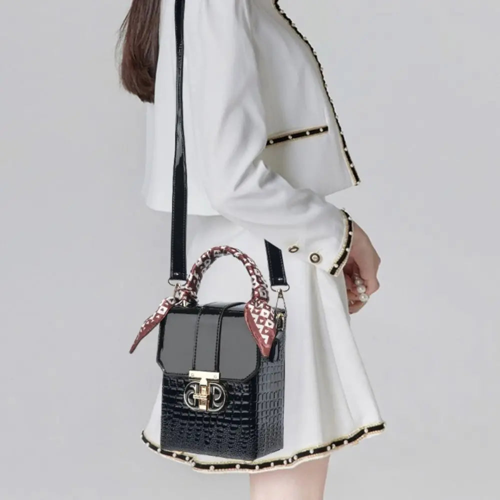 Person holding a black handbag with a patterned strap against a plain background