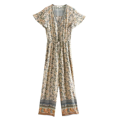 A short-sleeve V-neck jumpsuit with an all-over floral and paisley print in beige, brown, and muted blue, featuring a self-tie waist and patterned cuffs.