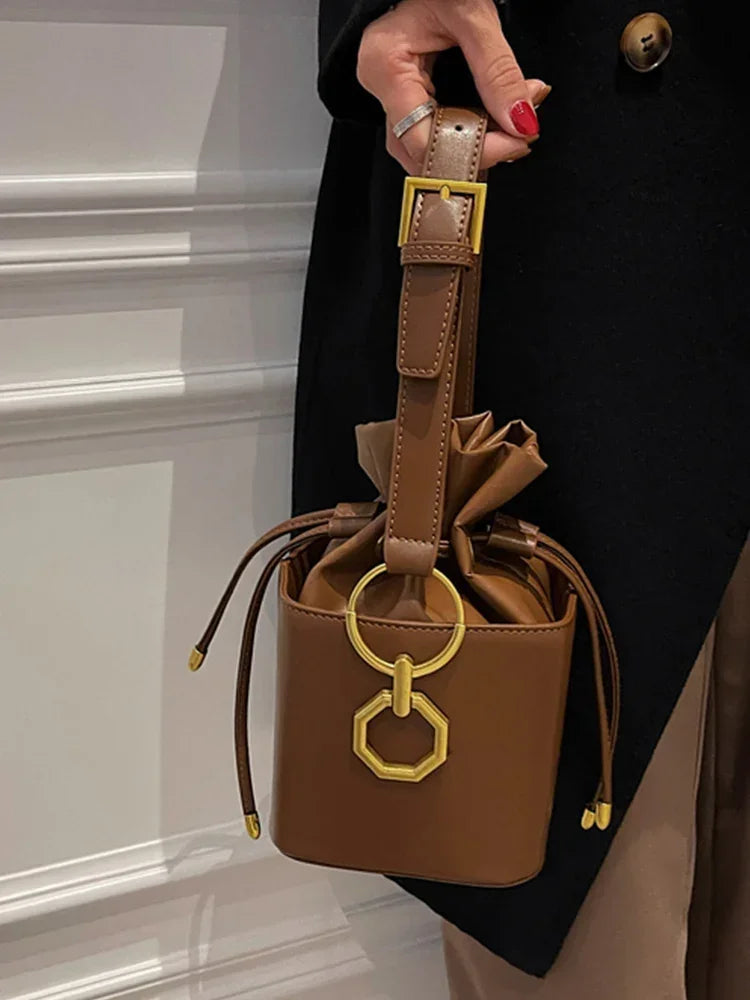 Brown leather handbag with gold accents held by a person wearing a black coat.