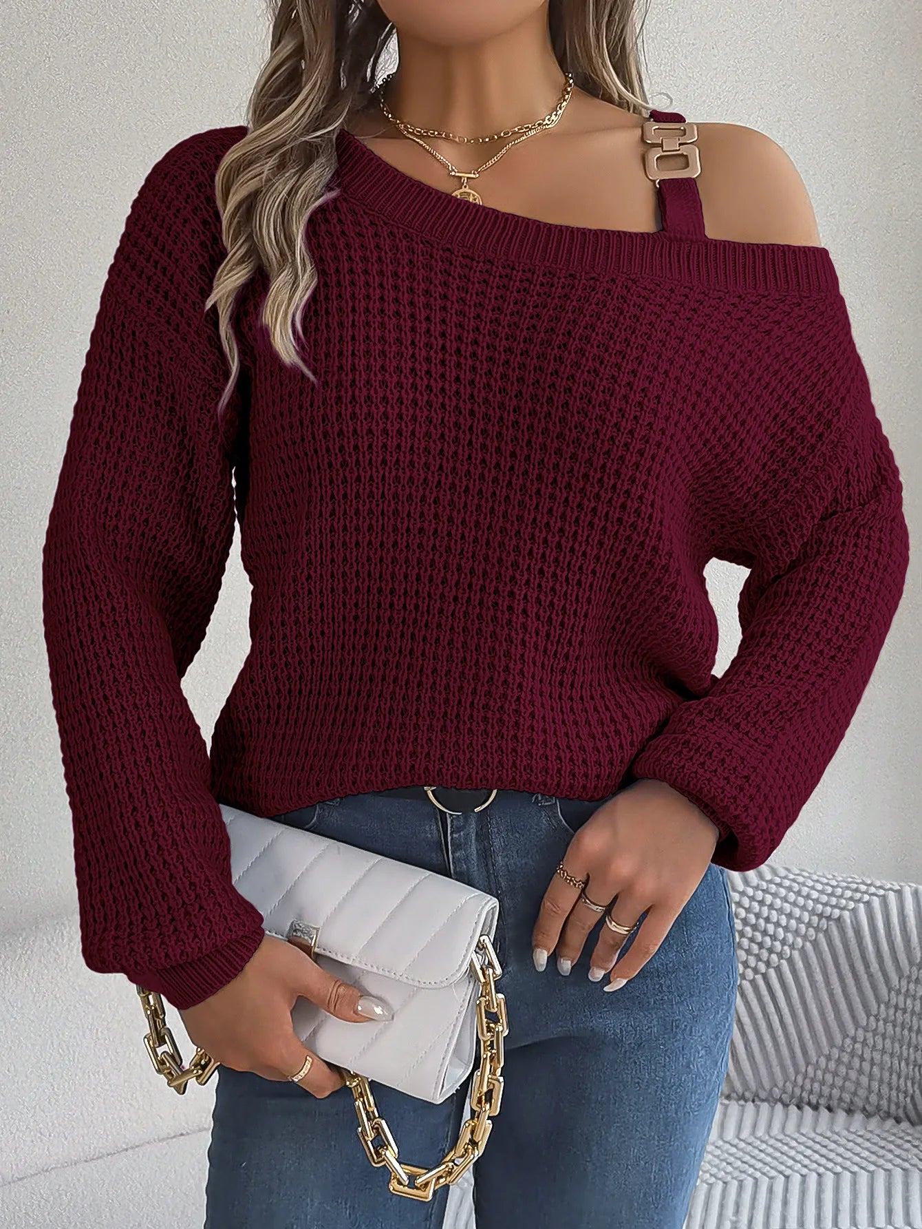 Woman wearing a burgundy off-shoulder sweater holding a white clutch with gold chain.