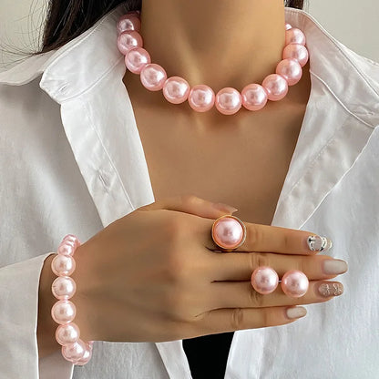 Person wearing a pink pearl necklace, bracelet, and ring with a white shirt.
