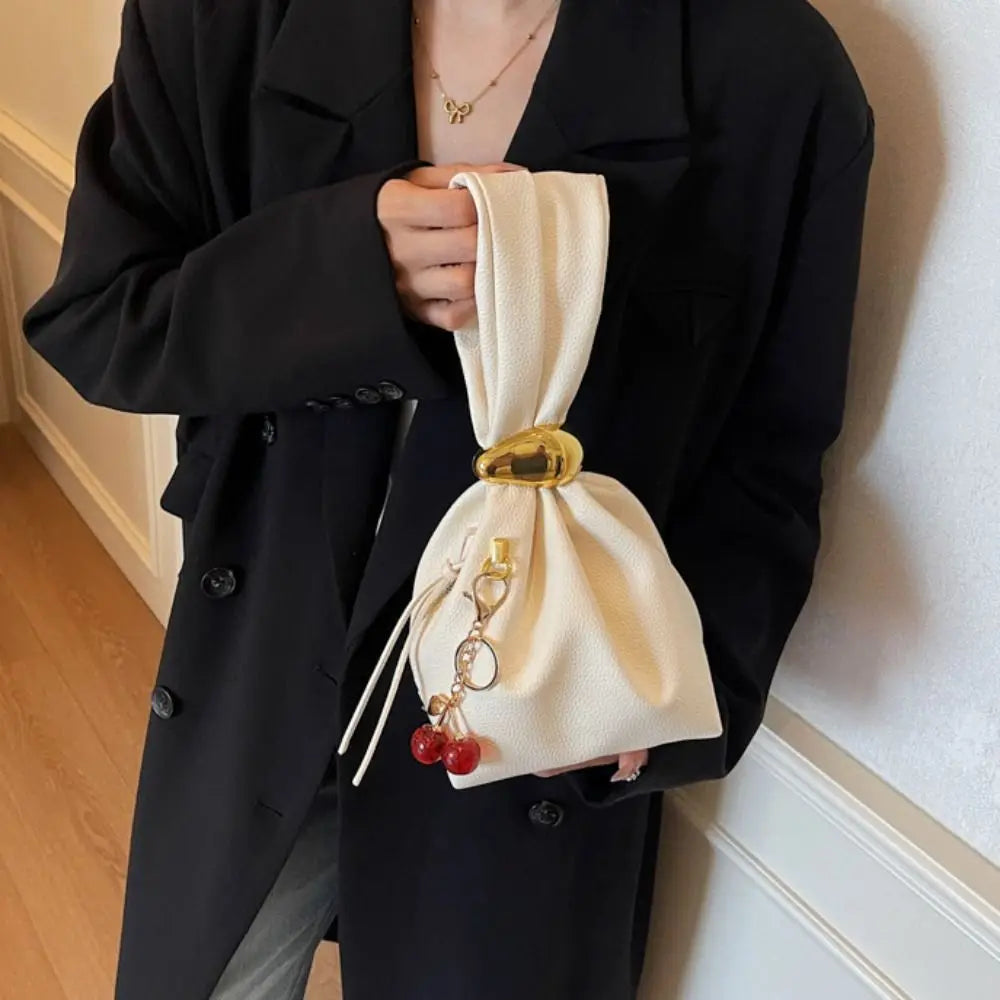 Person holding a beige drawstring bag with a gold buckle and red charms against a neutral background