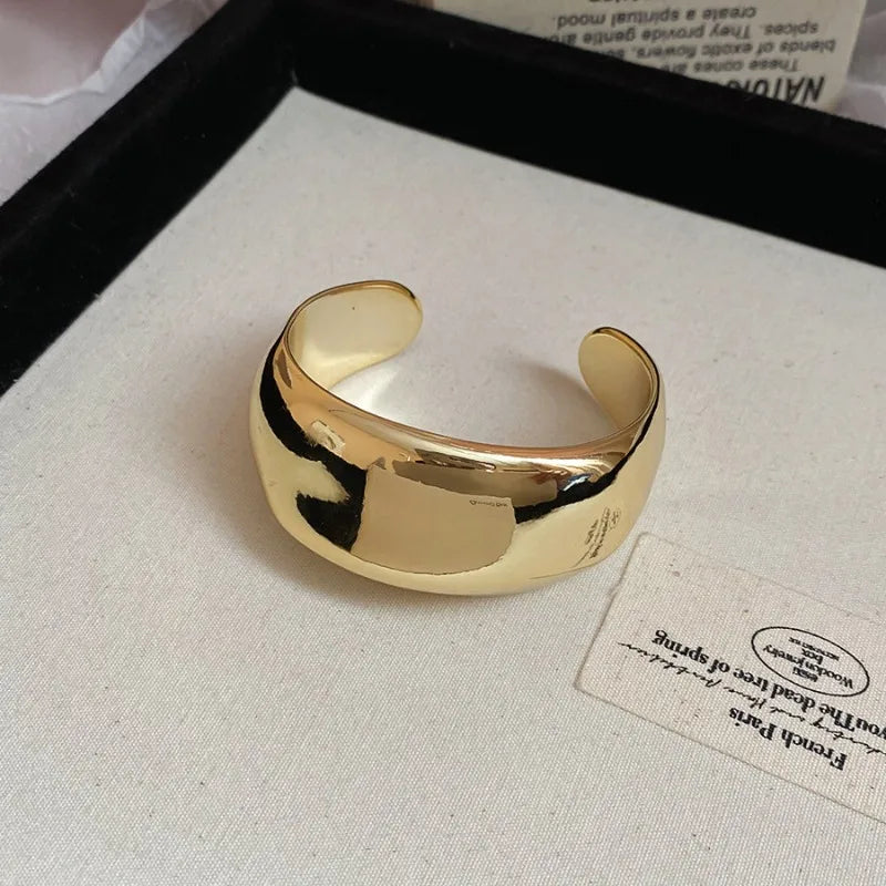 Gold open cuff bracelet on a light fabric background with a card.