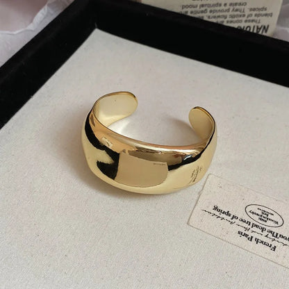 Gold open cuff bracelet on a light fabric background with a card.