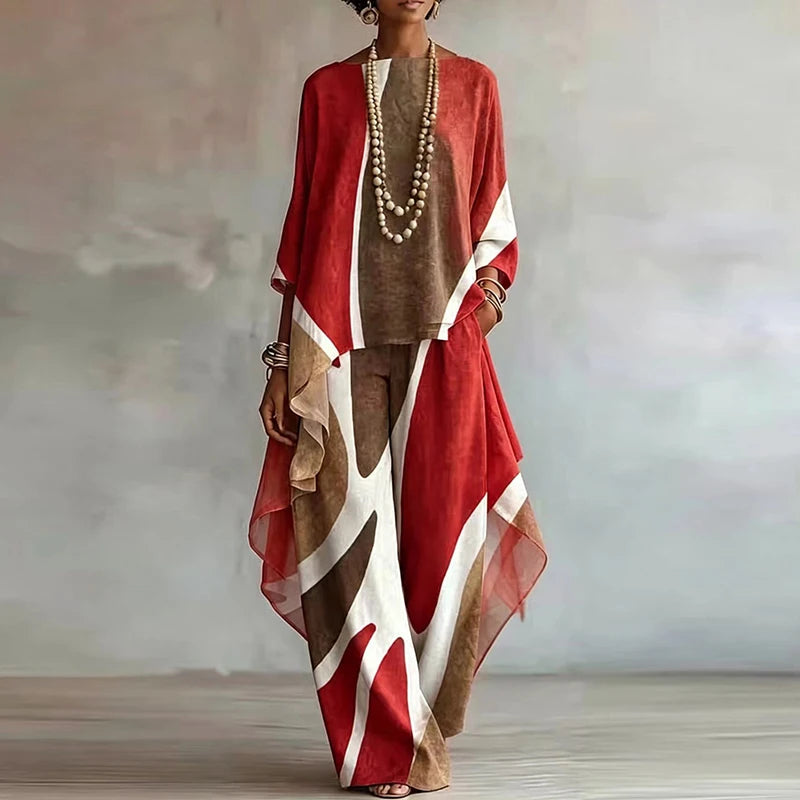A woman models a loose, bohemian-style two-piece outfit featuring a rust red, brown, and white abstract print. The set includes a long-sleeve top and matching wide-leg trousers, styled with a long beaded necklace and bracelets against a soft gray studio backdrop.