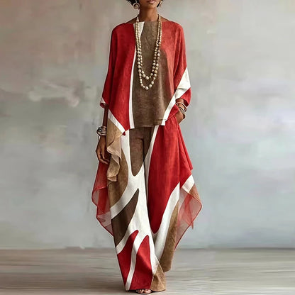 A woman models a loose, bohemian-style two-piece outfit featuring a rust red, brown, and white abstract print. The set includes a long-sleeve top and matching wide-leg trousers, styled with a long beaded necklace and bracelets against a soft gray studio backdrop.
