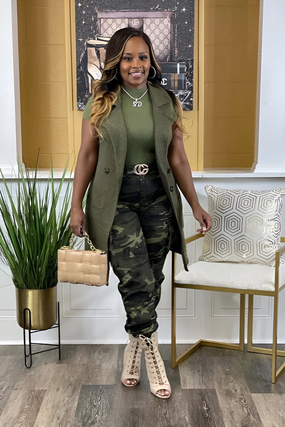 Woman in green vest and camouflage pants standing in a stylish room with decor elements.